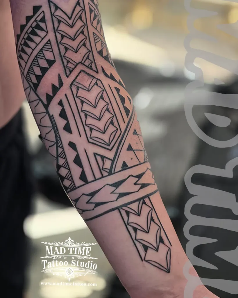 Sharp blackwork Polynesian tribal tattoo wrapping tightly around a forearm with geometric line work.
