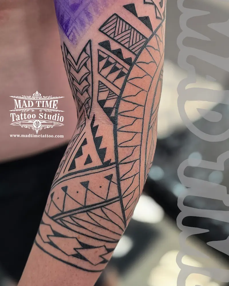 Close-up of a black ink Maori inspired tattoo on the inner arm with heavy geometric shading and triangles.