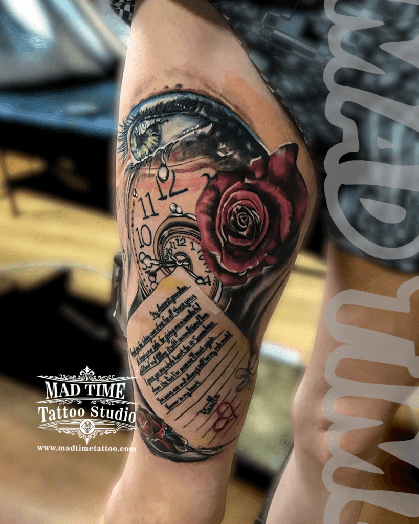 colour-realism-tattoos-liverpool Highly detailed color realism tribute tattoo featuring a realistic human eye with a green iris, a vintage pocket watch, a deep red rose, and a scroll letter dedicated to a grandmother signed by Paulina, inked by Mad Time Tattoo.