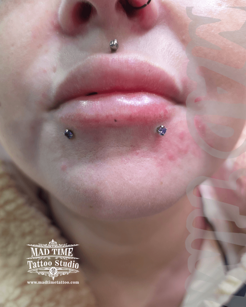 Close-up of a glamorous oral piercing setup by Mad Time Tattoo Studio, showcasing lower lip snake bites using sparkling blue gemstone crystal studs, paired with a classic medusa philtrum stud.