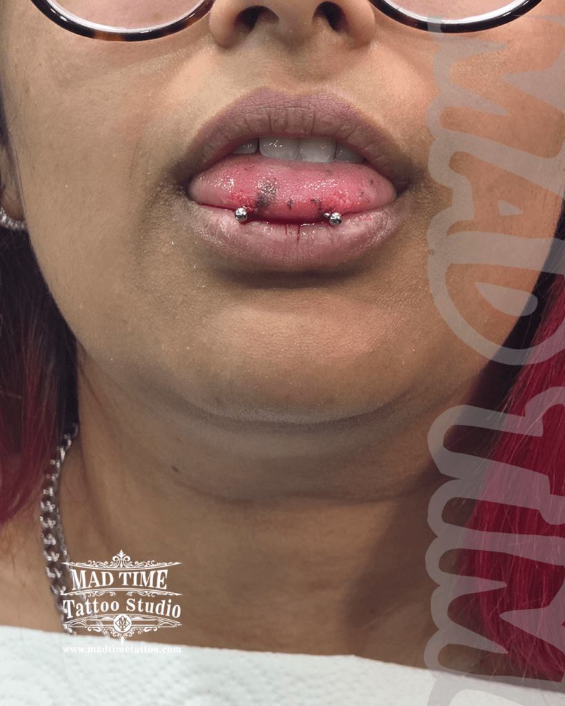 Freshly mapped classic silver snake eyes tongue piercing at Mad Time Tattoo Studio, showing high-polished titanium ball ends with professional surgical marking guides visible on a client's tongue.