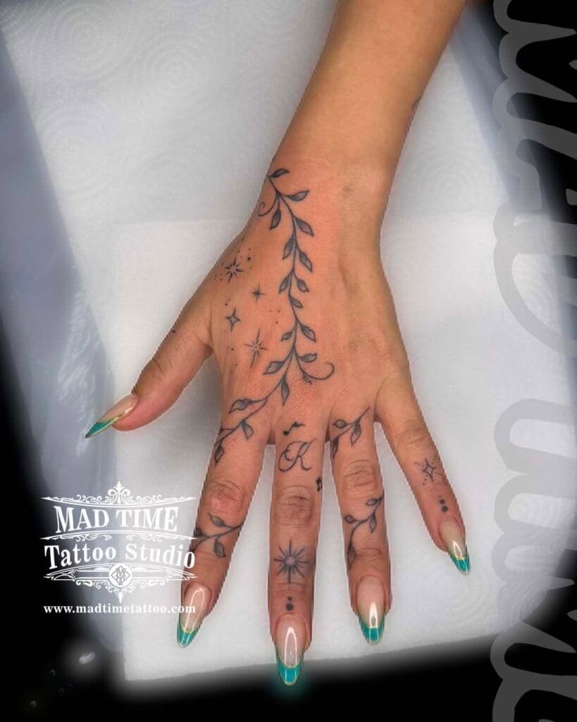 Delicate fine line botanical tattoo wrapping across the back of a woman's hand and fingers.