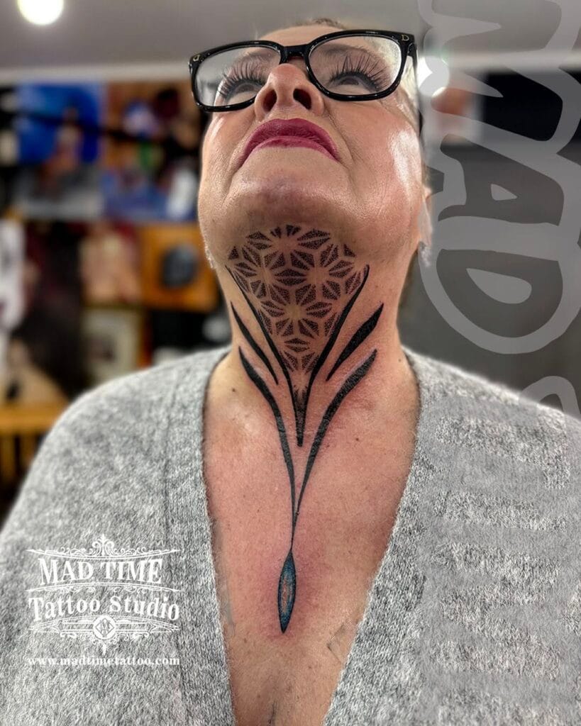 Front view of a bold blackwork and dotwork neck tattoo on a woman covering the throat and chin with a symmetrical geometric pattern and tapering ornamental lines.
