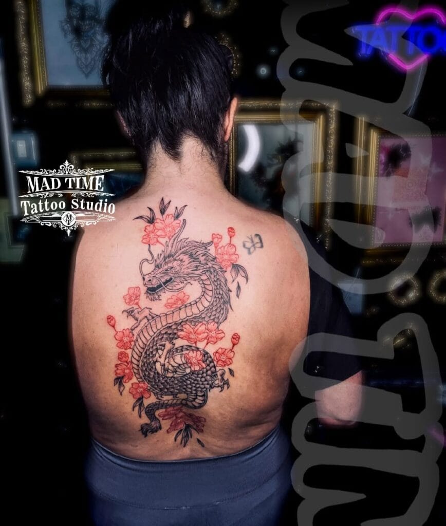 Massive full back dotwork tattoo of a traditional Japanese dragon (Ryu) wrapping around a woman's back and spine, surrounded by vibrant red cherry blossom flowers.