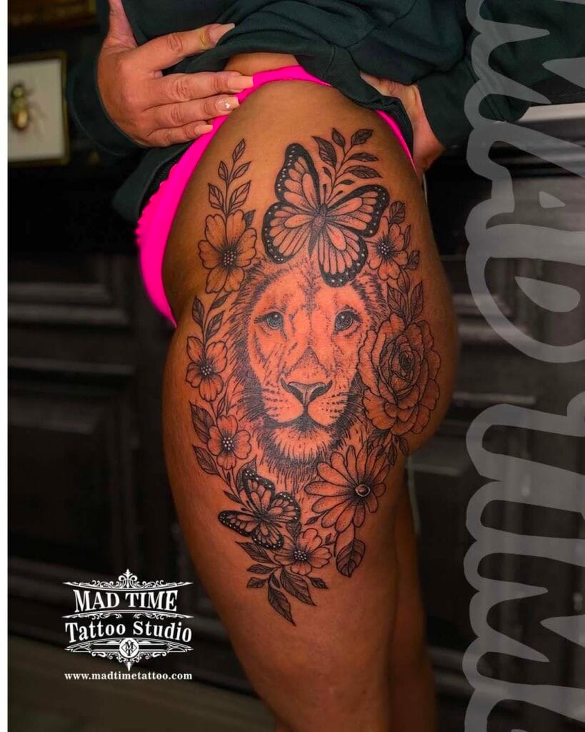 Ornamental dotwork tattoo of a lion's head blended with a butterfly and flowers on a woman's thigh.