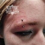 36Professional Piercing Liverpool home new ognialna zagubiona 36 kafelkow Professional eyebrow piercing showcase at Mad Time Tattoo Studio, featuring a classic curved titanium barbell with silver metal beads on a female client's eyebrow arch.