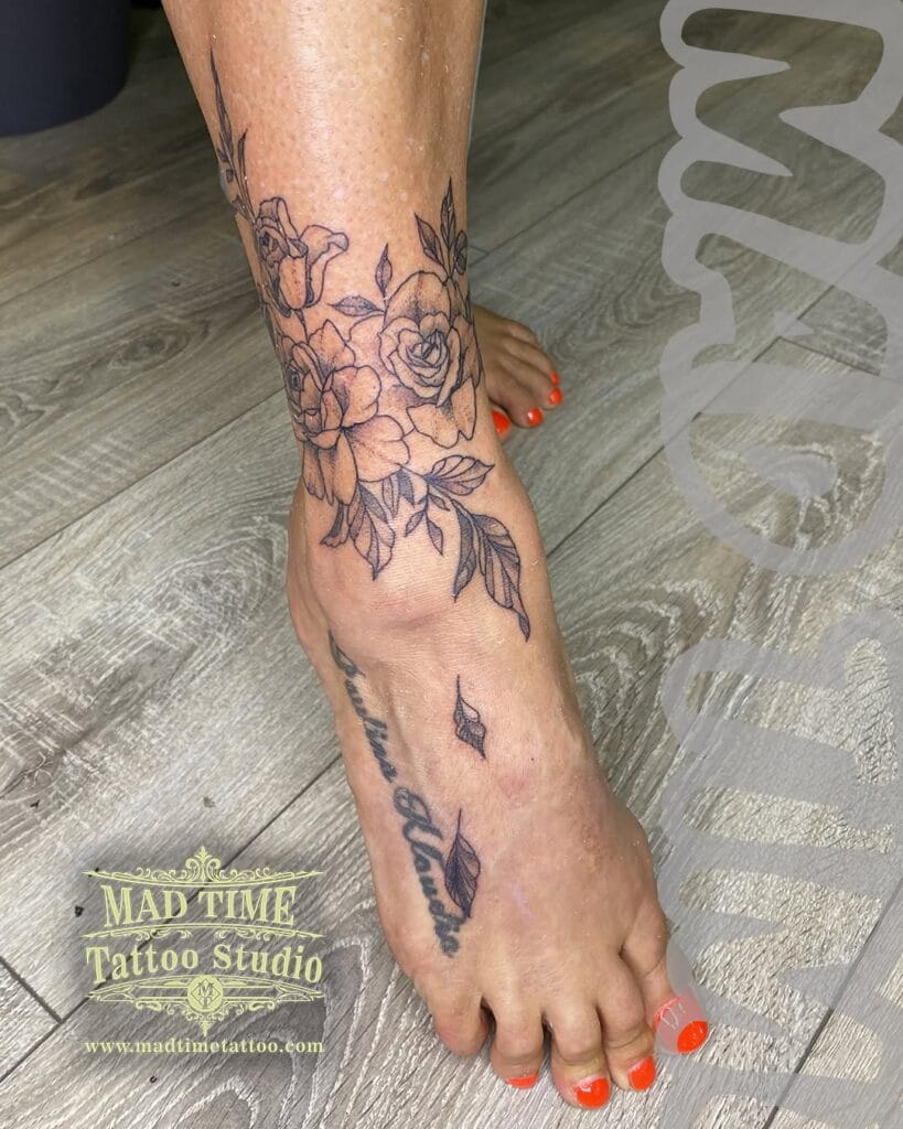 Dainty fine line botanical tattoo wrapping around a foot and ankle with tiny leaves and delicate shading.