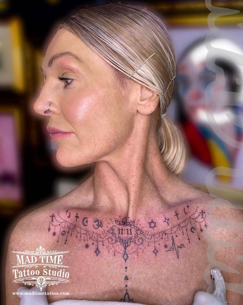 Elegant fine line ornamental tattoo sprawling across a woman's chest and collarbone area.