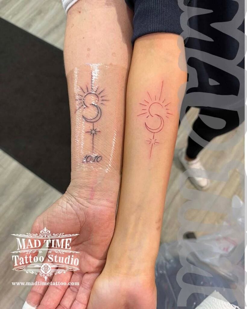 Matching minimal fine line red ink tattoos on two forearms featuring delicate celestial and floral symbols.