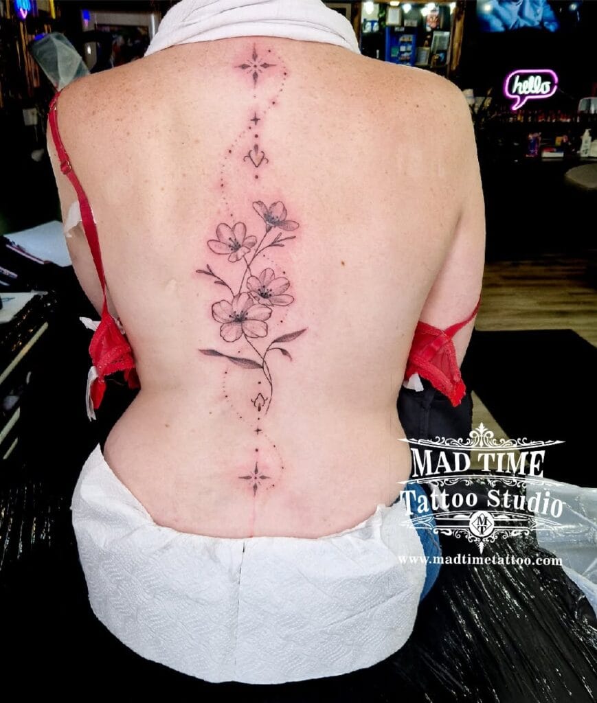 Feminine fine line cherry blossom branch tattoo climbing vertically up a woman's spine.
