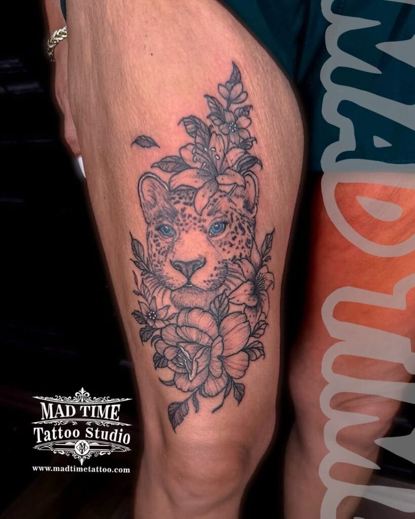 Detailed fine line lion portrait tattoo on a thigh surrounded by delicate blooming flowers.