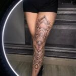Home new Massive black and grey ornamental tattoo covering a woman's entire front leg from thigh to ankle, featuring layered geometric mandalas, shaded flowers, and a small Taurus zodiac symbol.