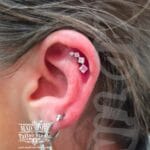36Professional Piercing Liverpool home new ognialna zagubiona 36 kafelkow Professional helix piercing showcase at Mad Time Tattoo Studio, featuring an elegant curved cluster jewelry piece with clear and pink square crystals on a female client's upper ear cartilage.