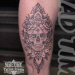 Home new Black and grey tattoo of a human skull embedded inside a complex geometric mandala pattern on the outer thigh and side of the leg.