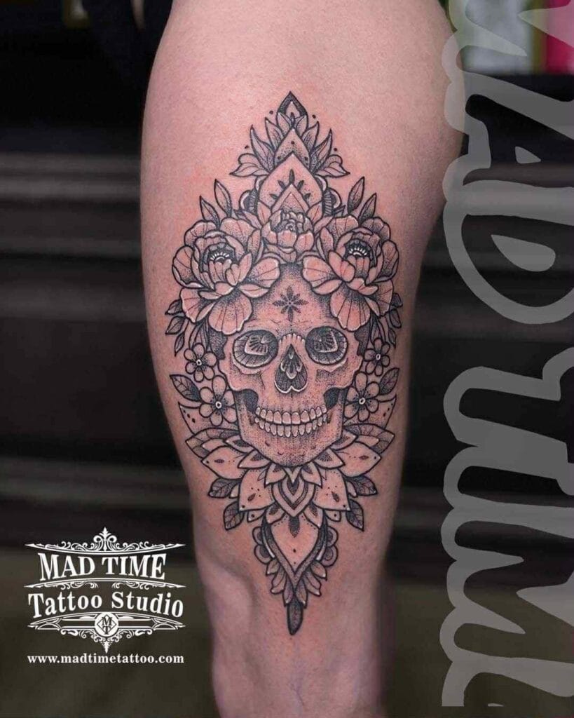 Black and grey tattoo of a human skull embedded inside a complex geometric mandala pattern on the outer thigh and side of the leg.