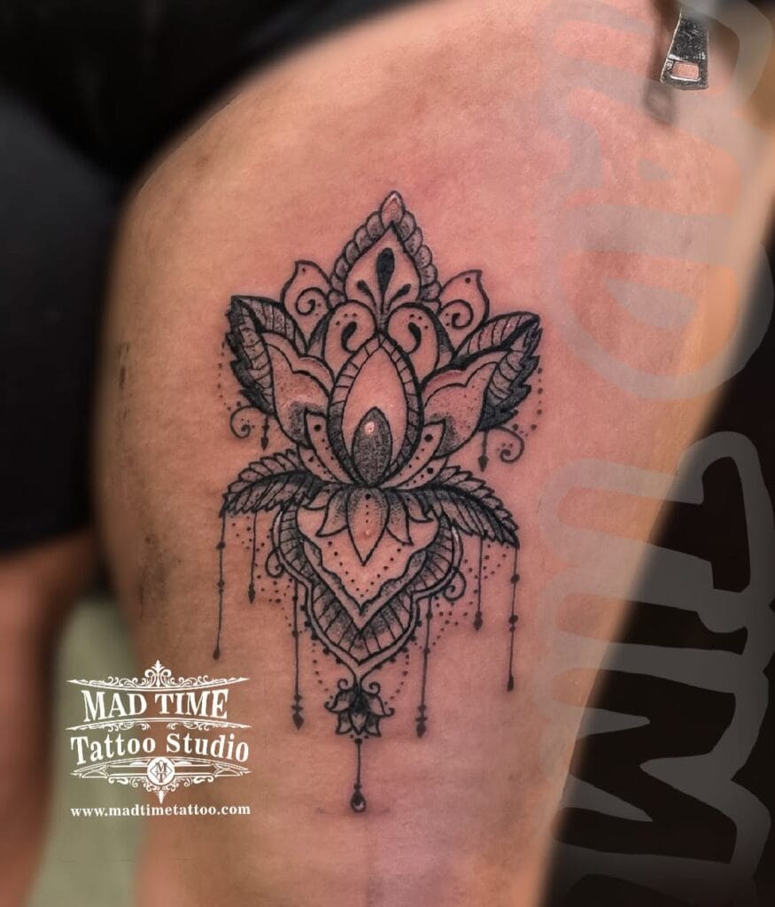 Ornate mandala lotus flower tattoo with dangling crystal beads on a woman's thigh and upper hip area.