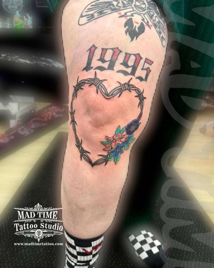 Traditional black ink tattoo above the knee showing a barbed wire heart with the birth year 1995 custom typography.
