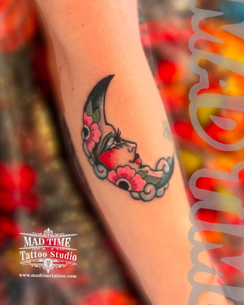 Colorful traditional tattoo of a crescent moon with a woman's face and red roses on a shoulder.