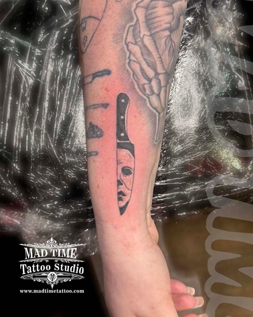Blackwork traditional tattoo on a forearm shaping a kitchen knife with piercing woman's eyes inside the blade.