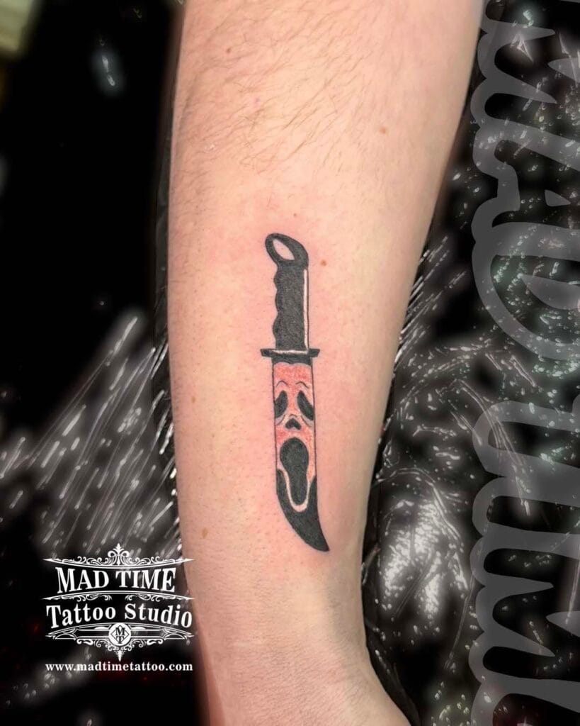 Black and grey forearm tattoo of a classic dagger featuring the Ghostface mask from the Scream movie inside the blade.