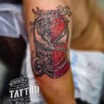 Home new Dynamic color and blackwork realism tattoo of a split portrait showing half Spider-Man face and half Venom symbiote face with sharp teeth on a man's upper arm by Mad Time Tattoo.