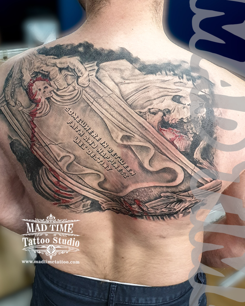 Custom black and grey realism upper back tattoo depicting a stone tomb skull effigy with a ribbon banner script reading Somewhere In Between Faith And Happiness Lies Destiny by Henry at our studio