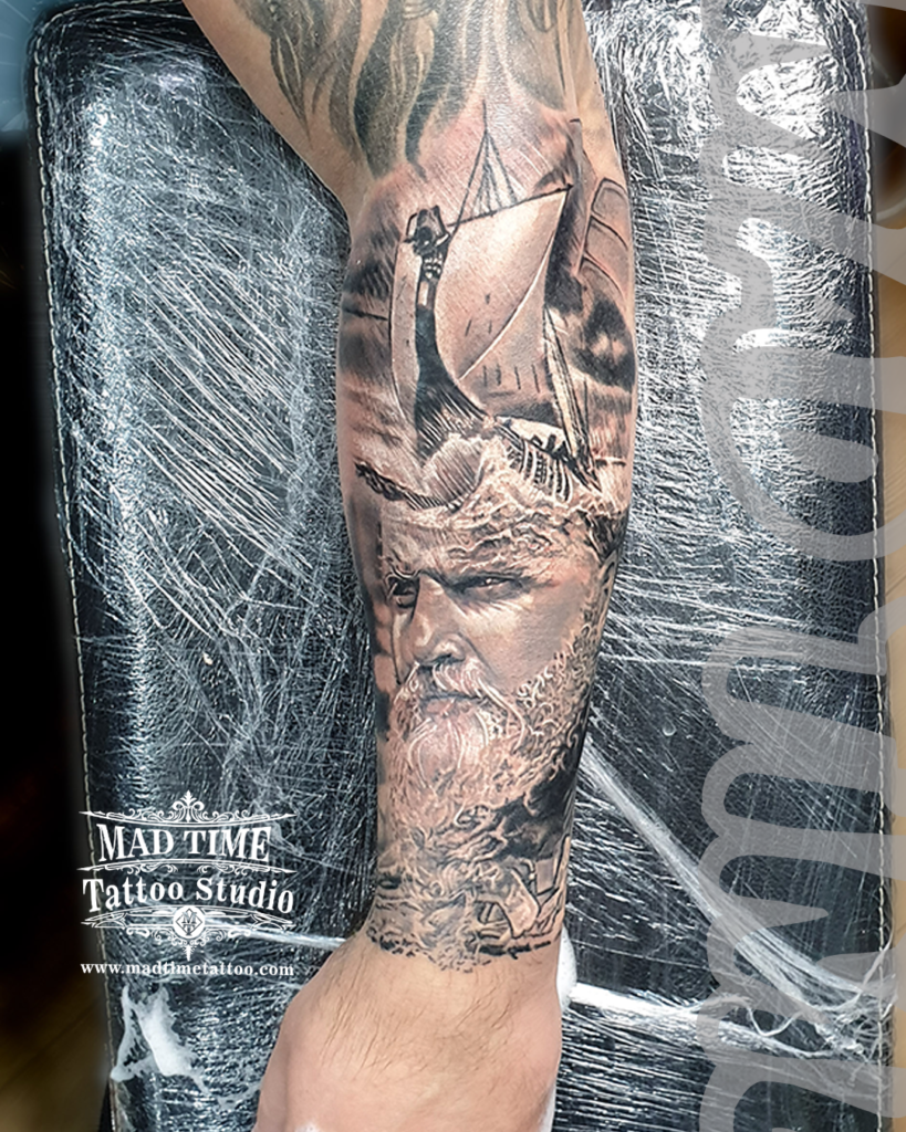 • Detailed black and grey realism forearm tattoo featuring a powerful Norse sea god Poseidon with a textured white beard beneath a crashing Viking drakkar longship by resident artist Henry at our studio