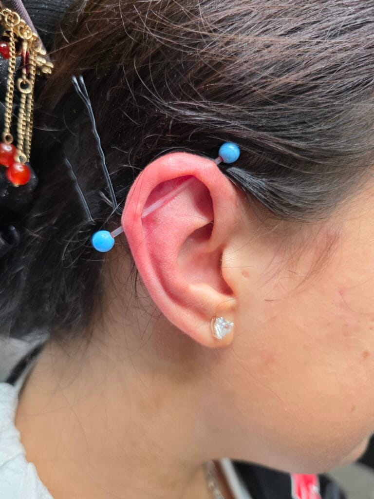 Transparent industrial piercing barbell with light blue acrylic beads on the ends and a heart lobe stud
