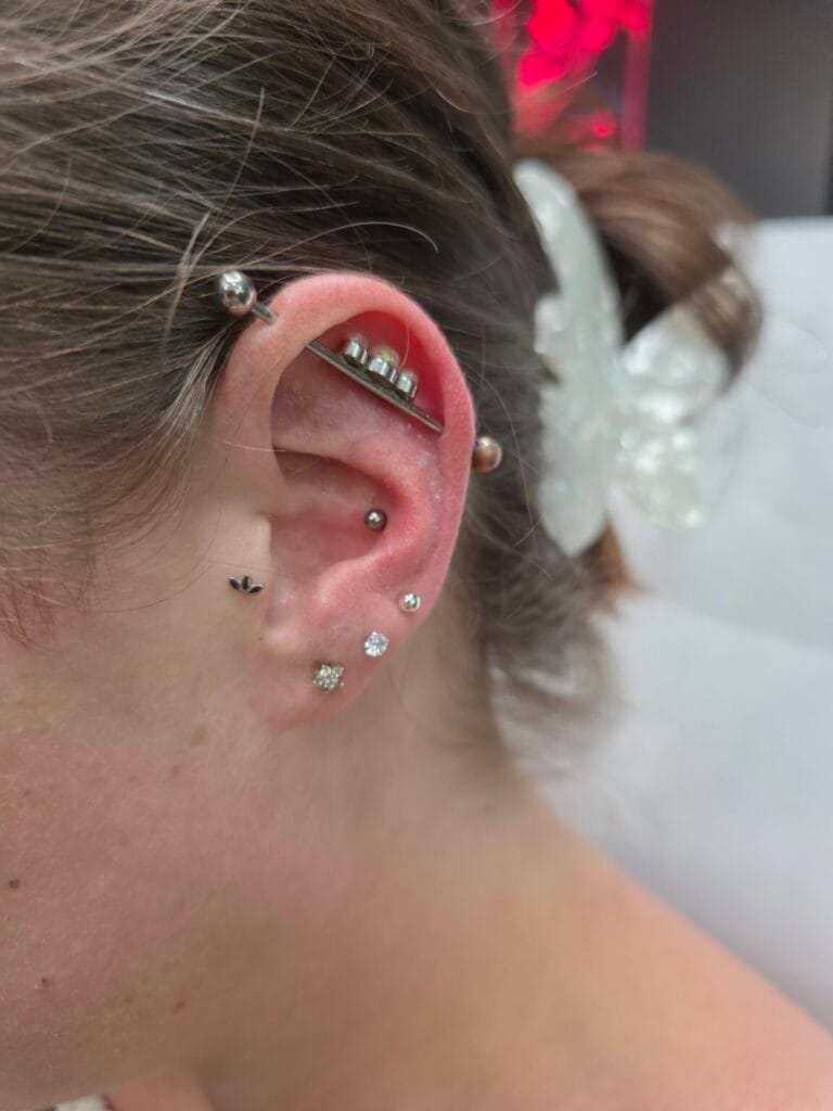 Silver titanium industrial piercing barbell with three white pearls and a crystal charm paired with a rook and triple lobe piercing