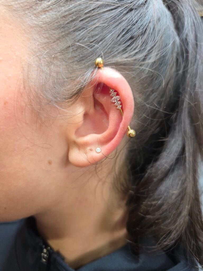 Gold industrial piercing barbell with a central marquise-cut crystal cluster on the ear cartilage rim
