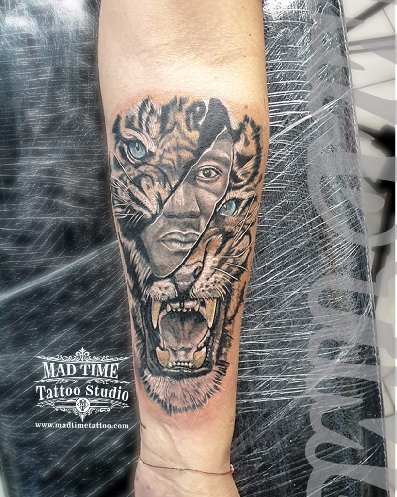 Double exposure forearm realism tattoo morphing a roaring tiger's face with a human woman's portrait featuring bright blue eyes by Henry at our studio