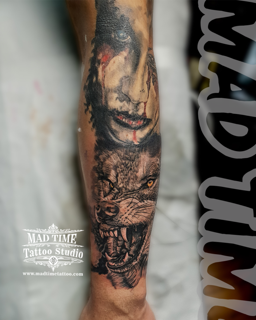 Close up forearm view of a dark realism horror tattoo showing a bleeding woman's face above a snarling wild wolf with orange eyes by Henry at our studio