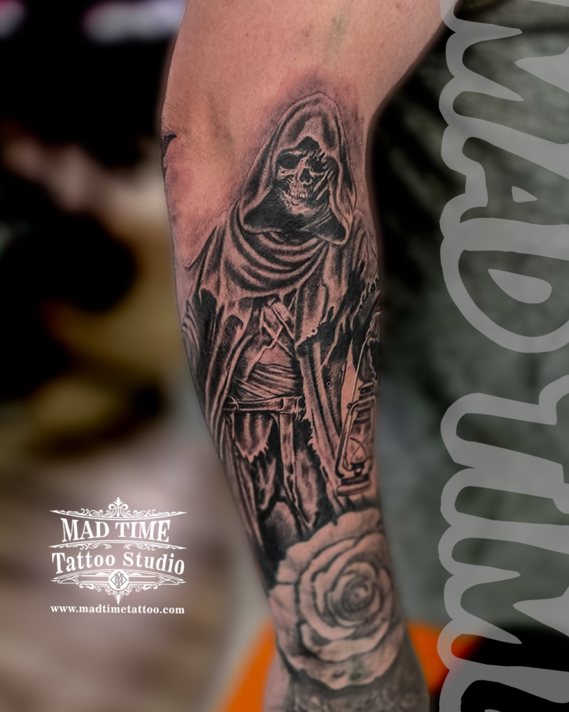 Black and grey dark realism tattoo of a hooded Grim Reaper skull holding a vintage oil lantern above a soft rose by Henry at our studio