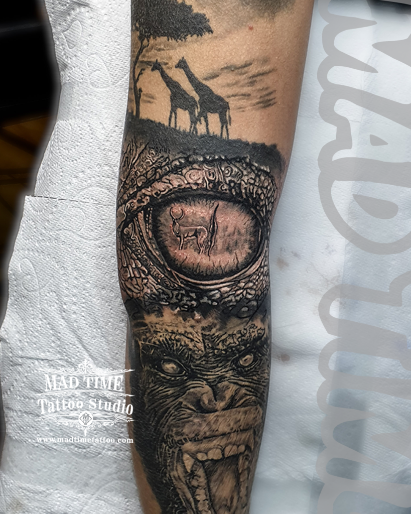 Close up view of a black and grey realism forearm tattoo featuring a reflection of a gazelle in a detailed animal eye and a snarling gorilla by Henry at Mad Time Tattoo Studio