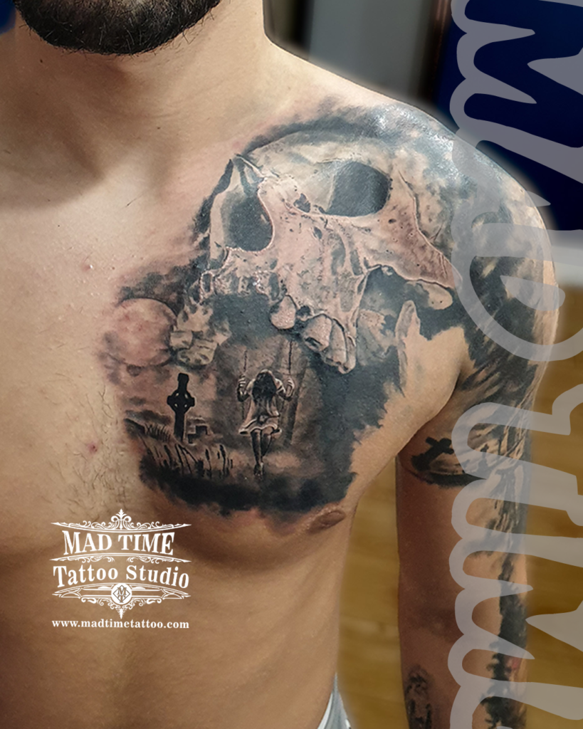 Dramatic surrealism chest tattoo combining a giant skull profile with a gothic graveyard scene and a girl on a swing by Henry at our studio