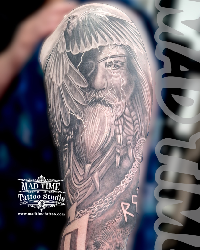 • Black and grey realistic Odin tattoo on upper arm with detailed beard crow wings and white lightning bolts by resident artist Henry at our studio