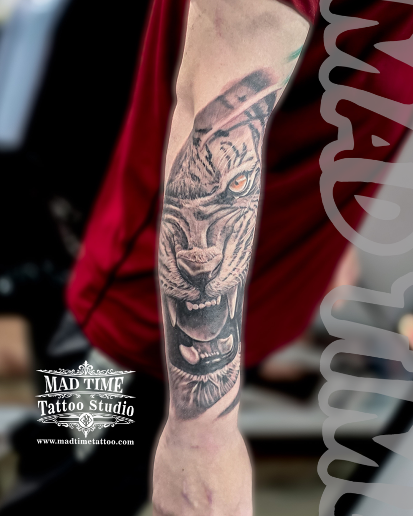 Black and grey realism roaring tiger tattoo on forearm featuring custom amber colour eyes by resident artist Henry at our studio