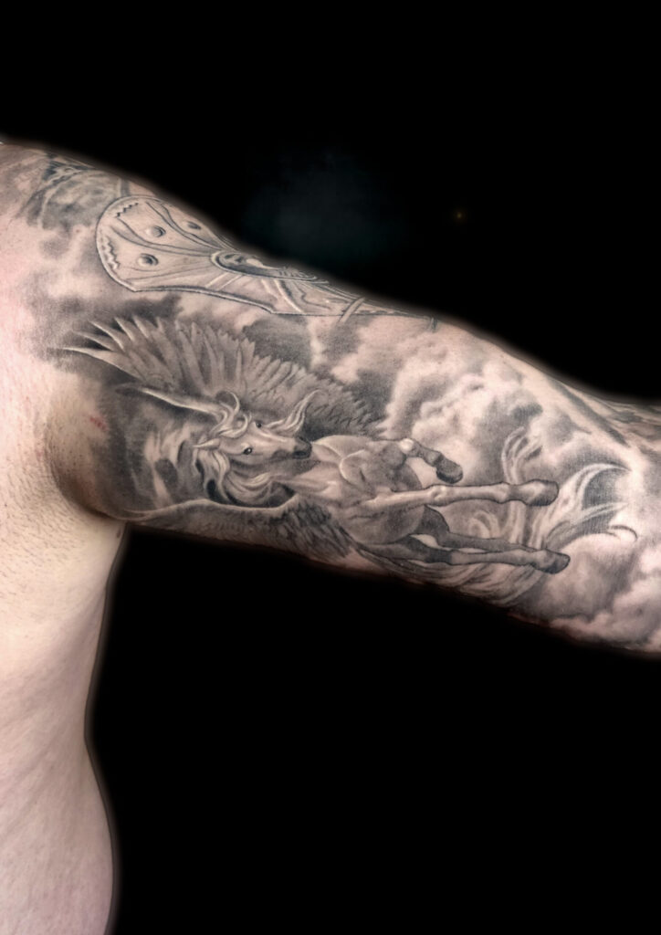 Realistic black and grey flying Pegasus tattoo with detailed wings and cloud background by guest artist Pablo from Spain at our studio