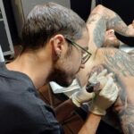 Guest Artists at Mad Time Tattoo main Guest artist Pablo from Spain in glasses focused on tattooing a realistic rose and custom chest piece at our studio