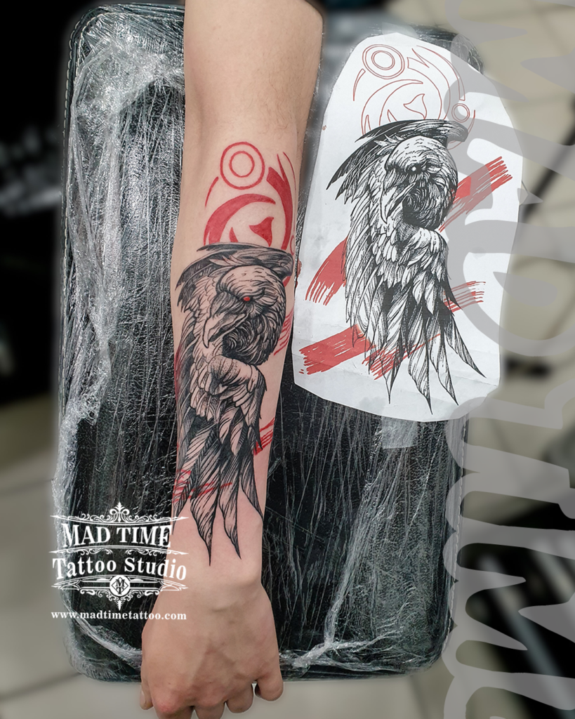 Trash Polka raven tattoo on a forearm featuring scratch line wings and a geometric red circle next to the original paper artwork sketch by our studio