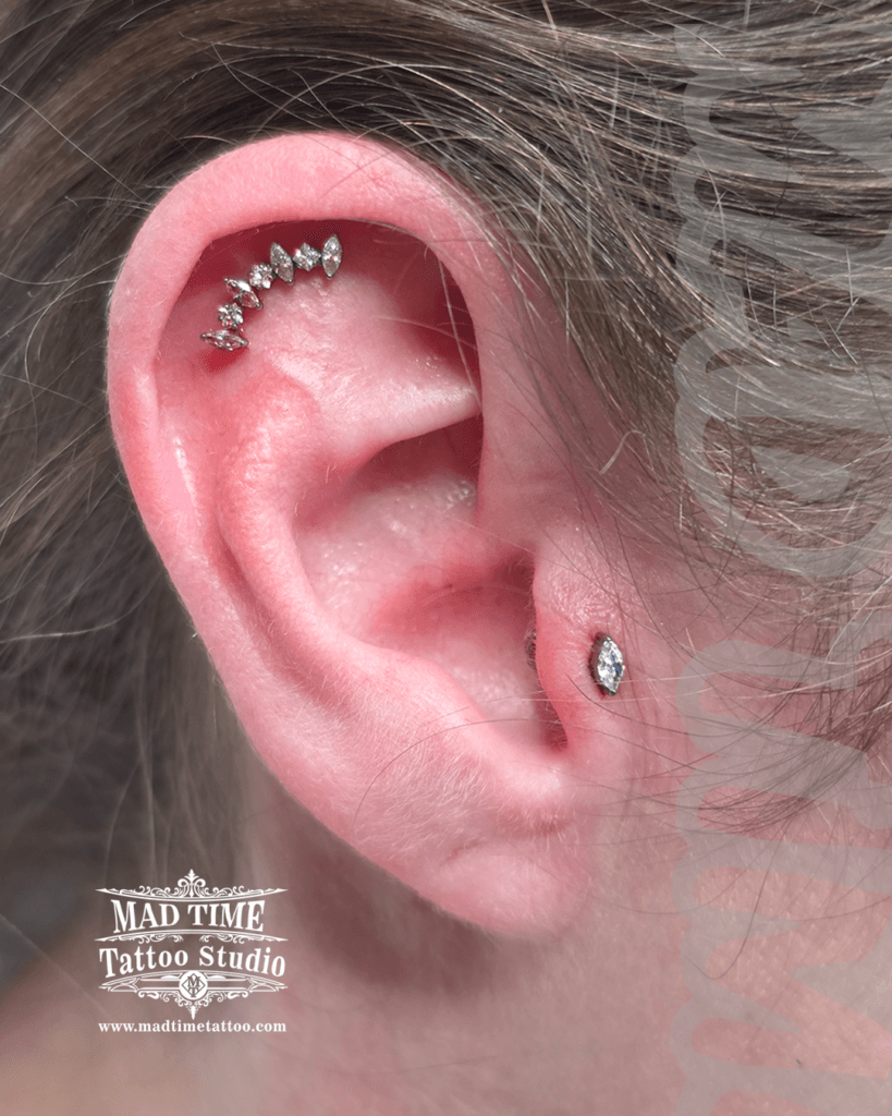 Silver helix piercing with a five-stone marquise crystal cluster and a matching teardrop crystal tragus stud at Mad Time Tattoo Studio
