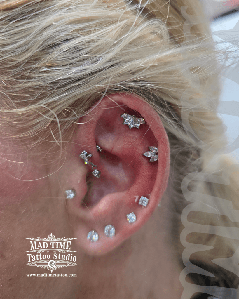 Complex ear curation featuring flat helix marquise leaf jewelry double forward helix conch and multiple lobe piercings at Mad Time Tattoo Studio