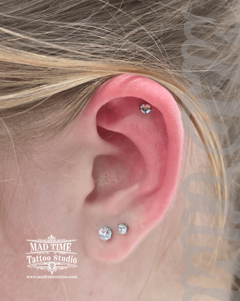 inimalist flat helix piercing with an iridescent Aurora Borealis crystal stud paired with double clear lobe earrings at Mad Time Tattoo Studio
