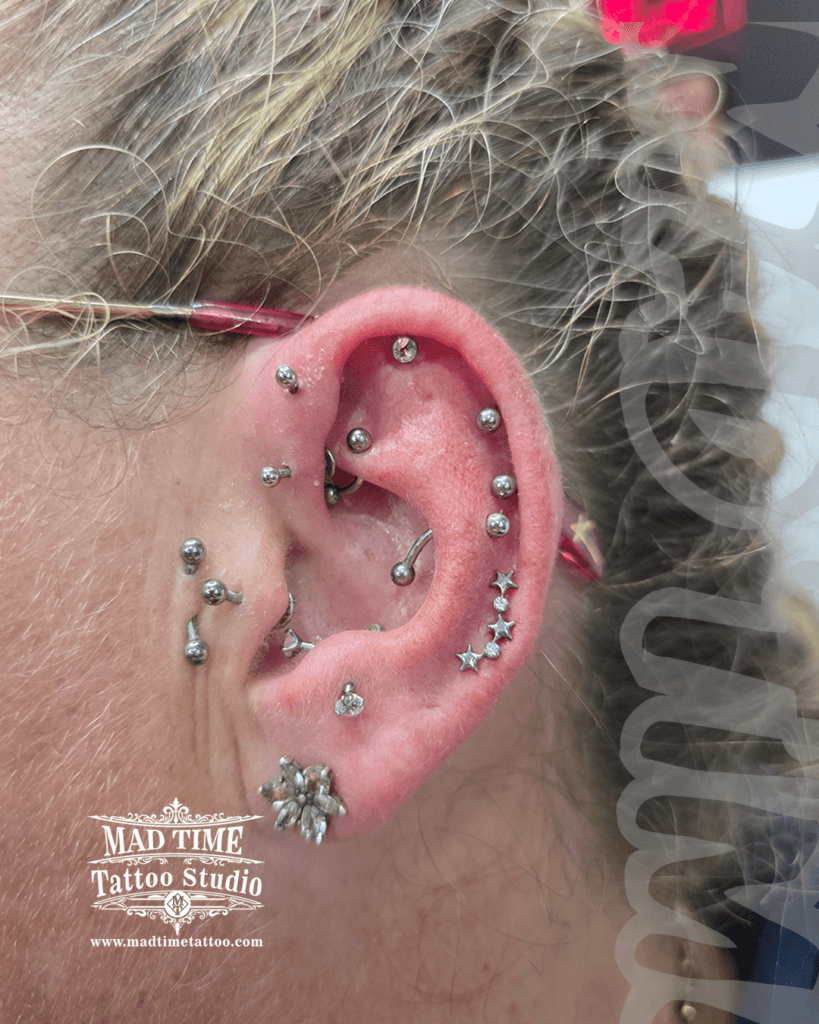 • Maximalist ear curation with a triple helix piercing using titanium balls alongside tragus conch and a star cluster bar at Mad Time Tattoo Studio