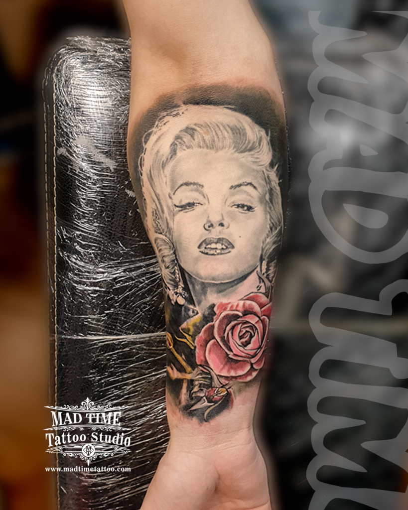 High contrast black and grey realism portrait tattoo of Marilyn Monroe paired with a realistic crimson red rose on a forearm by our studio