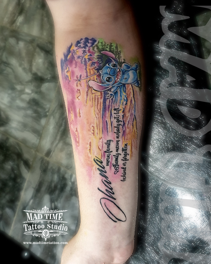 Vibrant watercolor style Disney Stitch tattoo on forearm with custom cursive Ohana script and family quote lettering by our studio